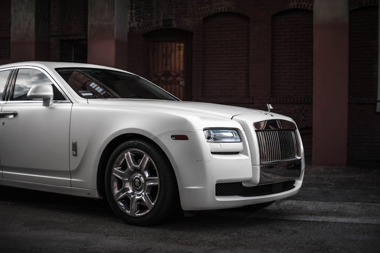 who-we-are-01 Elegant white Rolls Royce Ghost parked in a stylish urban backdrop, showcasing luxury and design.